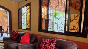 A living room with a brown sofa, red and black patterned cushions, and large windows with decorative iron bars. - Luxury Cozy Home in San Nicolas (San Miguel)