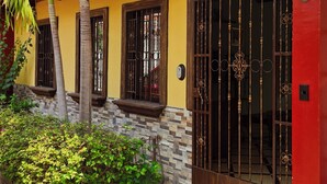 A house with a red door, a window with decorative bars, a stone wall, and a palm tree. - Luxury Cozy Home in San Nicolas (San Miguel)