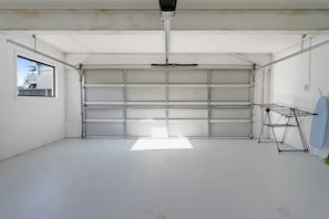 A garage with a closed metal door, a ceiling fan, and a clothes drying rack.