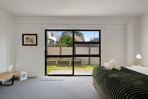 A bedroom with a bed, a bench, a fan, a picture on the wall, and a sliding door to a balcony.