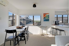 A modern kitchen with a dining area, large windows, and a view of the neighborhood.