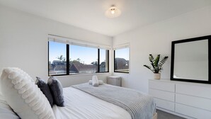 A bedroom with a bed, two windows, a potted plant, and a mirror on the wall.