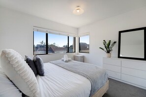 A bedroom with a bed, two windows, a potted plant, and a mirror on the wall.