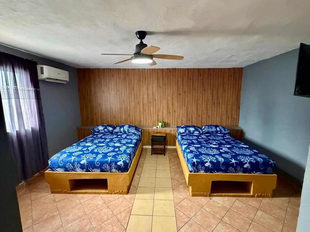 Une chambre avec deux lits, un ventilateur de plafond et une petite table.