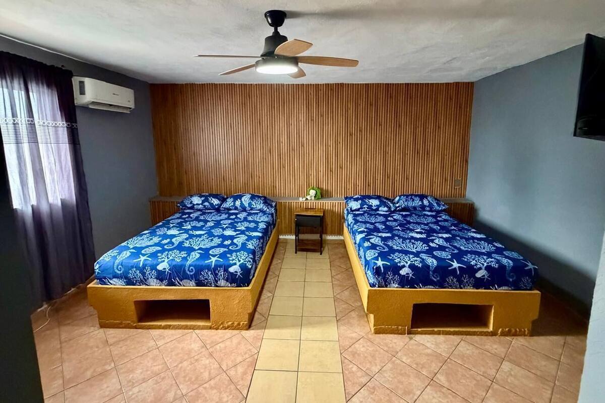 A room with two beds, a ceiling fan, and a small table.