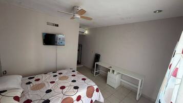 A bedroom with a bed, a desk, a ceiling fan, and a TV mounted on the wall.