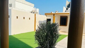 Una planta en maceta sobre un patio con baldosas y una vista despejada de un edificio al fondo.