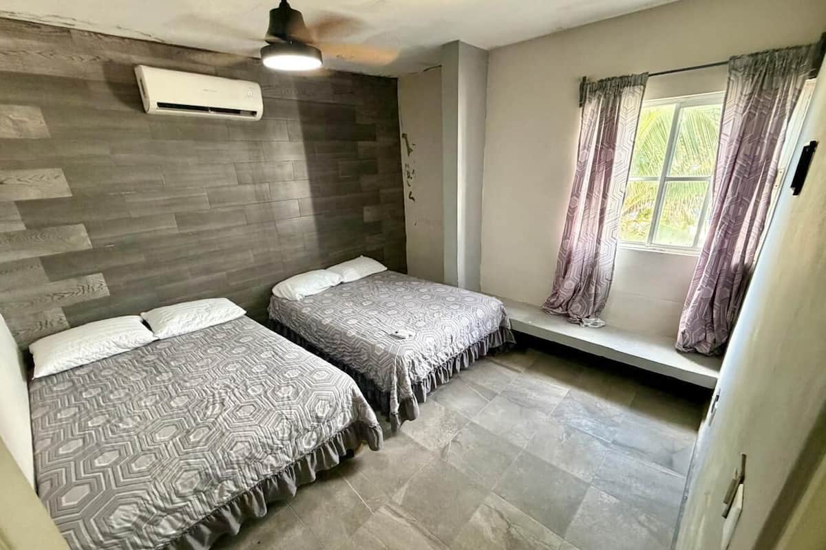 A bedroom with two beds, a window with curtains, a ceiling fan, and an air conditioning unit.