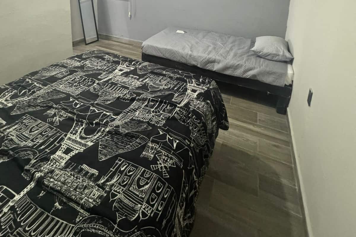 A small, dimly lit room with a bed, a TV mounted on the wall, and an air conditioner.