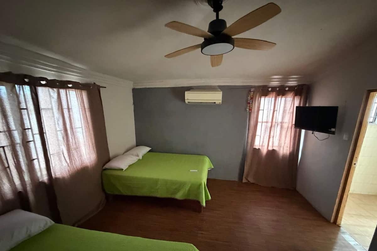 A room with two beds, a ceiling fan, an air conditioning unit, and a television on the wall.