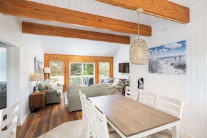Ein geräumiges Zimmer mit Holzbalkendecke, einem Esstisch mit Stühlen, einer Couch und einem Fernseher.
