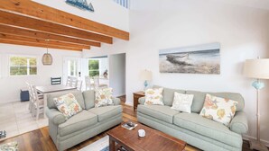 A spacious living room with a high ceiling, a dining area with a wooden table, and a view of the outdoors. - Coastal Getaway with Pool, Spa, Direct Beach Path! (Southern Shores)