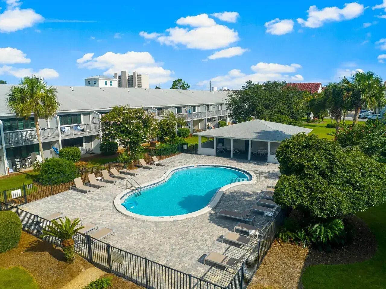 A swimming pool with lounge chairs, surrounded by greenery and a building with a flat roof.