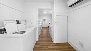 A laundry room with multiple washing machines, a wooden floor, and a white door at the end. - 30A Studio - Seaside/Pool/Beach Walking Distance (Santa Rosa Beach)