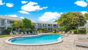 A swimming pool with lounge chairs, a tree, and a multi-story building in the background. - 30A Studio - Seaside/Pool/Beach Walking Distance (Santa Rosa Beach)