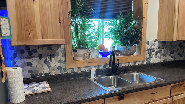 A kitchen with wooden cabinets, a granite countertop, a double sink, and a window with plants.