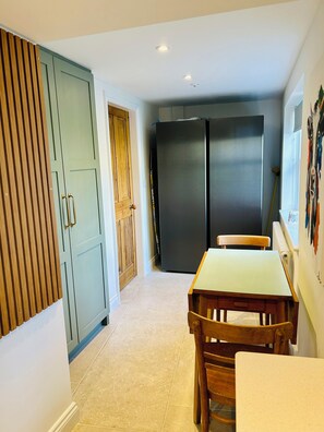 Eine kleine Küche mit Esstisch und Stühlen, einem Kühlschrank und einem Holzkorpus mit Tür.