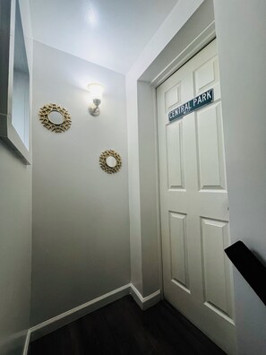 Un couloir avec une porte blanche portant l’inscription « Central Park West » et deux miroirs décoratifs fixés au mur.