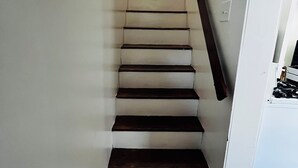 A staircase with wooden steps and a handrail, leading to a landing with a light switch and a wall-mounted light fixture.