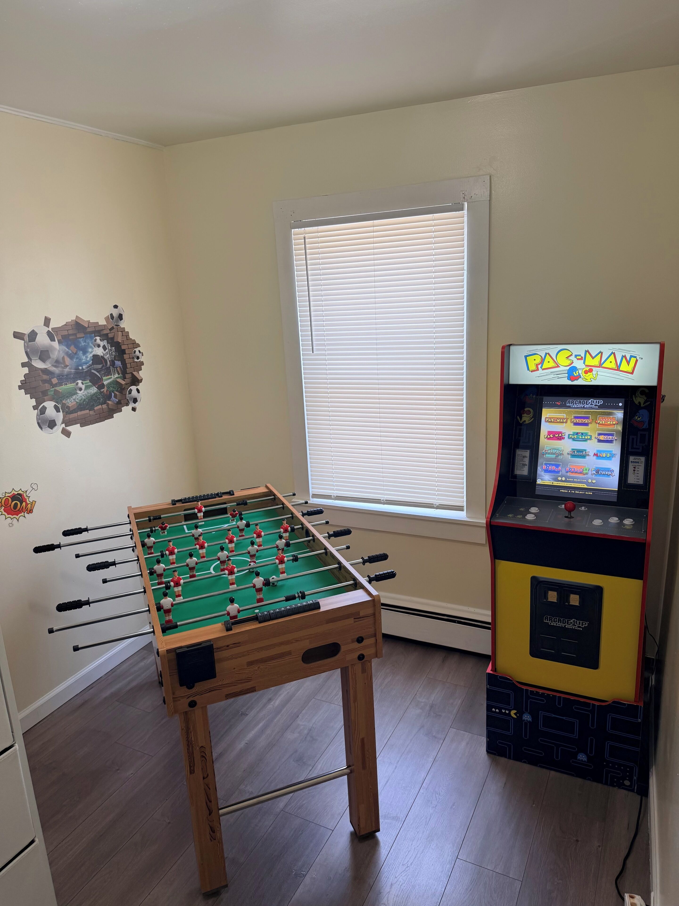 Una stanza con un tavolo da calcio balilla, un'arcade Pac-Man e una finestra con persiane.