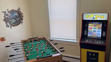 Una stanza con un tavolo da calcio balilla, un'arcade Pac-Man e una finestra con persiane.