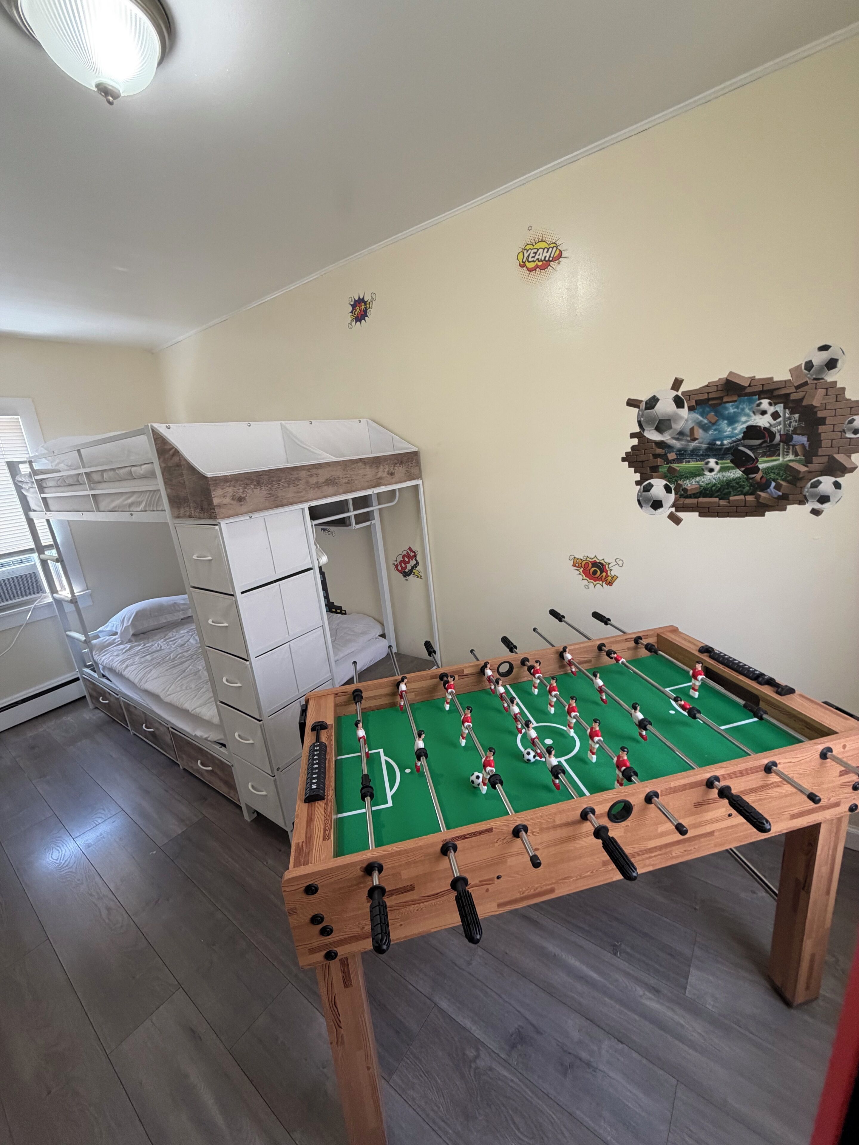 A room with a foosball table, bunk beds, and a wall with a soccer-themed mural.