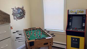 Ein Zimmer mit Kicker, Pac-Man Spielautomat und einem Fenster mit Jalousien.