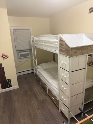 Une chambre avec un lit superposé, une fenêtre, un appareil de climatisation et un mur décoré avec des motifs de bandes dessinées.