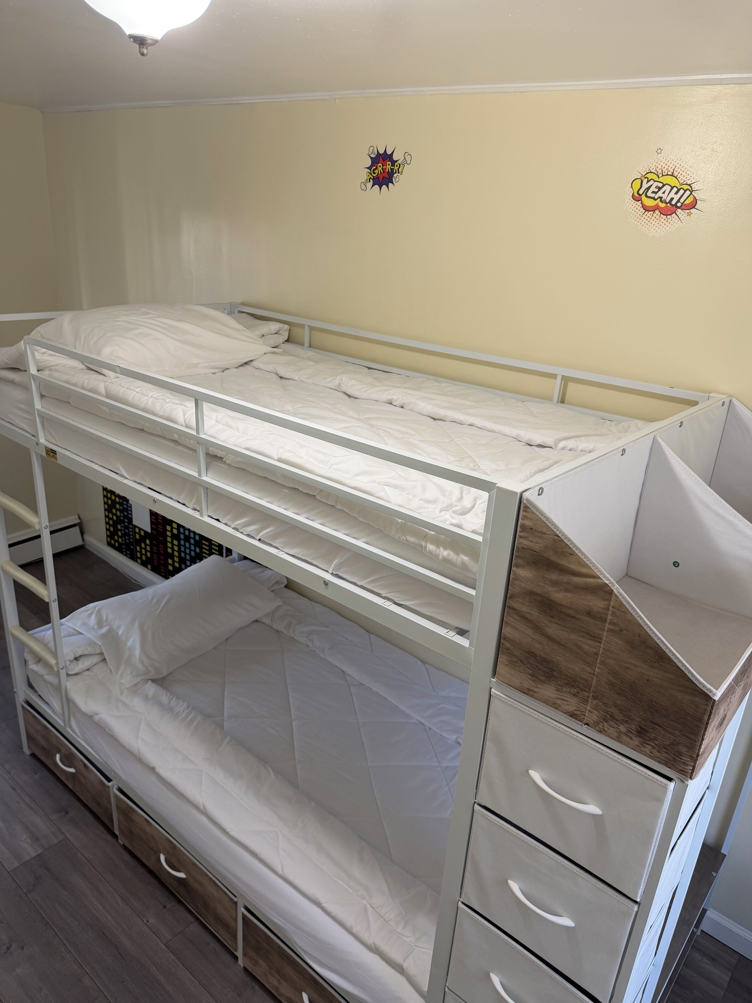 A bunk bed with drawers and a shelf, a wooden floor, and a wall with a comic book style sticker.