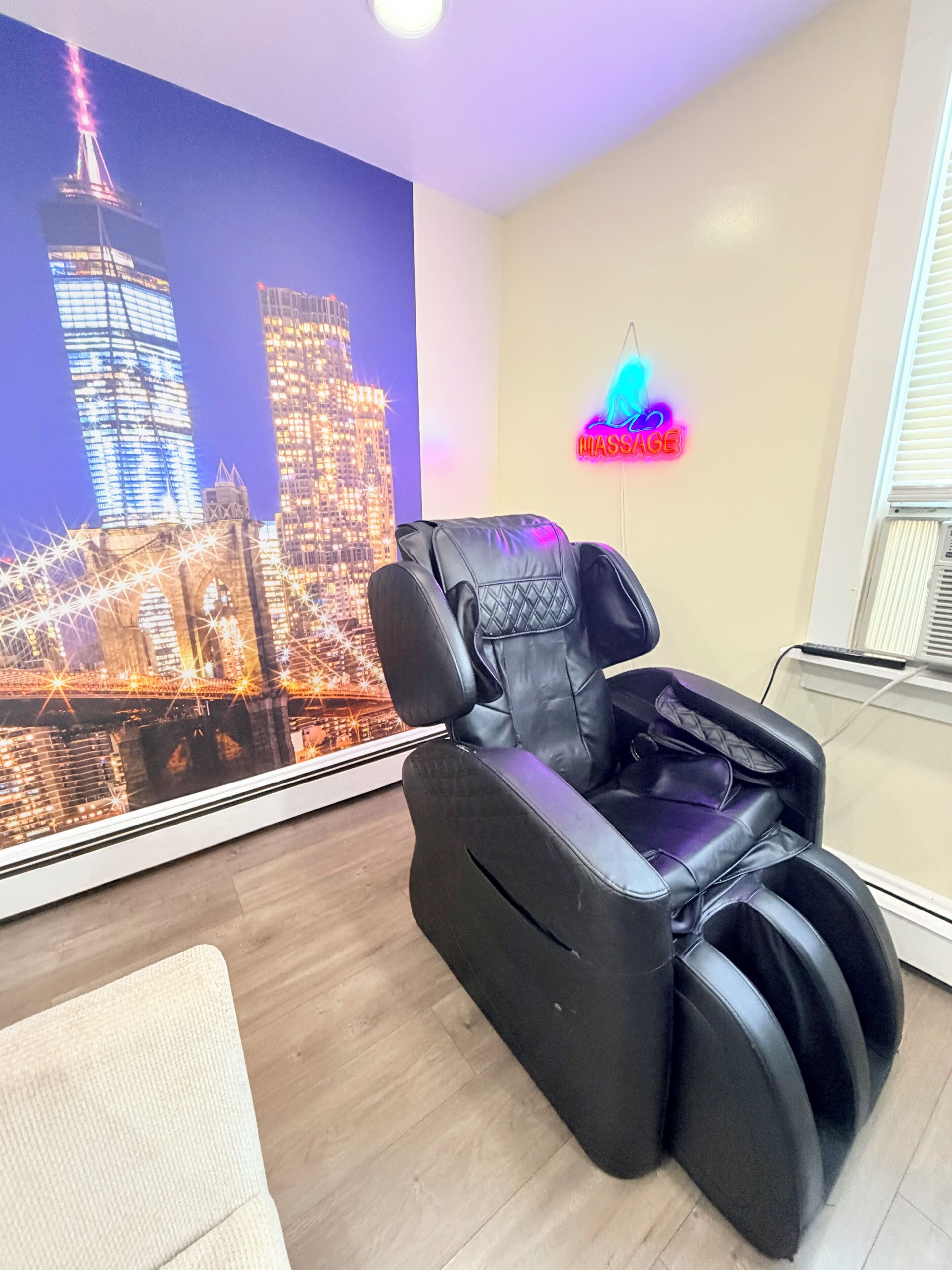 Un fauteuil de massage dans une pièce dont un mur est décoré d’une fresque représentant un paysage urbain et où l’on trouve un panneau lumineux au néon.