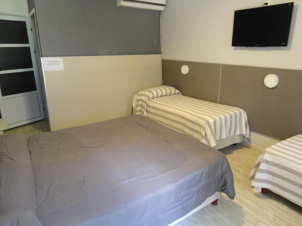 A room with two beds, a television, and a wall-mounted air conditioning unit.