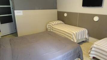 A room with two beds, a television, and a wall-mounted air conditioning unit.