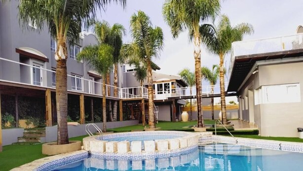 Una piscina con borde de azulejos, rodeada de palmeras y un edificio con balcones.