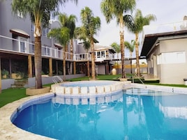 Una piscina con borde de azulejos, rodeada de palmeras y un edificio con balcones.