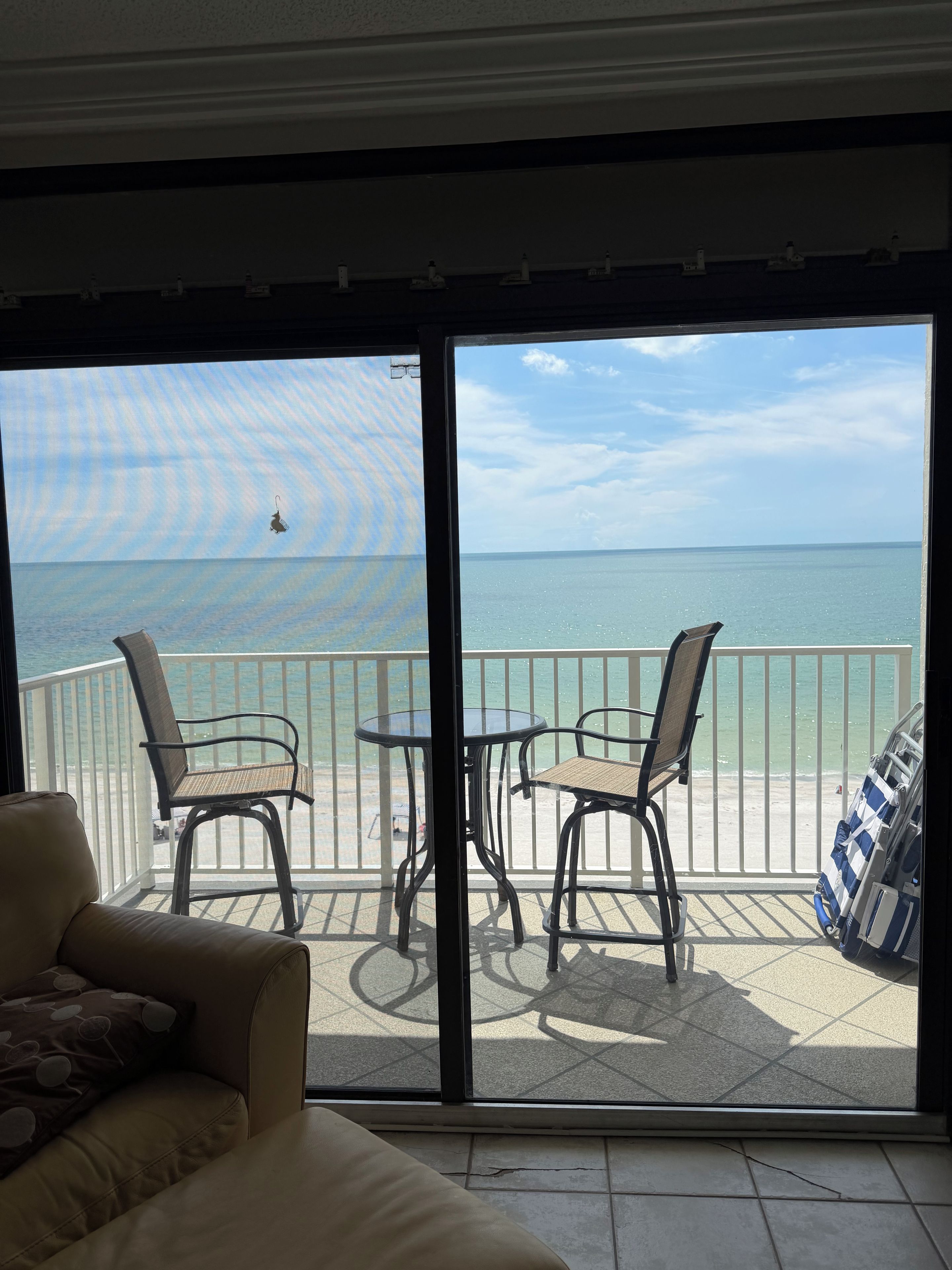 A balcony with a view of the beach and ocean, furnished with two chairs and a table.