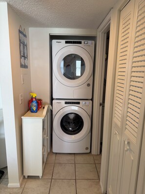 A compact laundry room with two stacked front-loading washers and a small cabinet with cleaning supplies. -  2-bedroom Gulf front condo private sandy white beach, unforgettable sunsets. (Indian Shores)