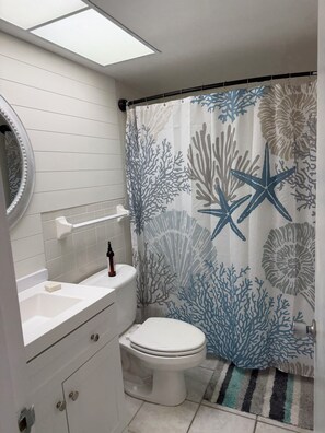 Un bagno con il water, un lavandino, uno specchio e una tenda da doccia con motivi di vita marina.