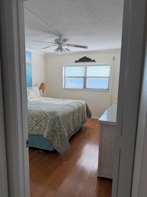 A bedroom with a bed, a ceiling fan, a window with blinds, and a wicker chair. -  2-bedroom Gulf front condo private sandy white beach, unforgettable sunsets. (Indian Shores)