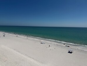 Une vaste plage de sable fin, sous un ciel bleu dégagé et une mer calme.