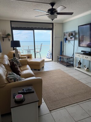 A living room with a sofa, a coffee table, a television, and a view of the ocean through a sliding glass door. -  2-bedroom Gulf front condo private sandy white beach, unforgettable sunsets. (Indian Shores)