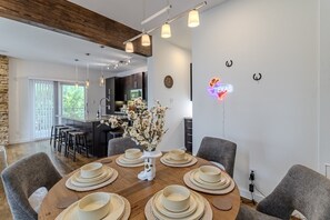 A modern dining area with a wooden table set for six, a vase of flowers, and a neon sign on the wall. - Chic 3-Story Retreat in Houston Heights (Houston)