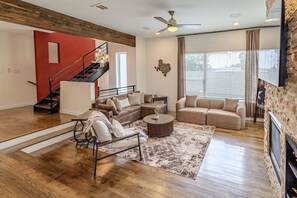 A spacious living room with a fireplace, a staircase, and a large window with curtains. - Chic 3-Story Retreat in Houston Heights (Houston)