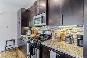 A modern kitchen with dark cabinetry, a stainless steel stove, a microwave, and a blender. - Chic 3-Story Retreat in Houston Heights (Houston)