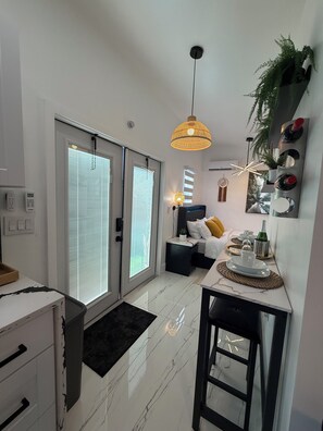 A modern kitchen with a dining area, a small side table, and a hanging light fixture. - Tropical Cottage (Greenacres)