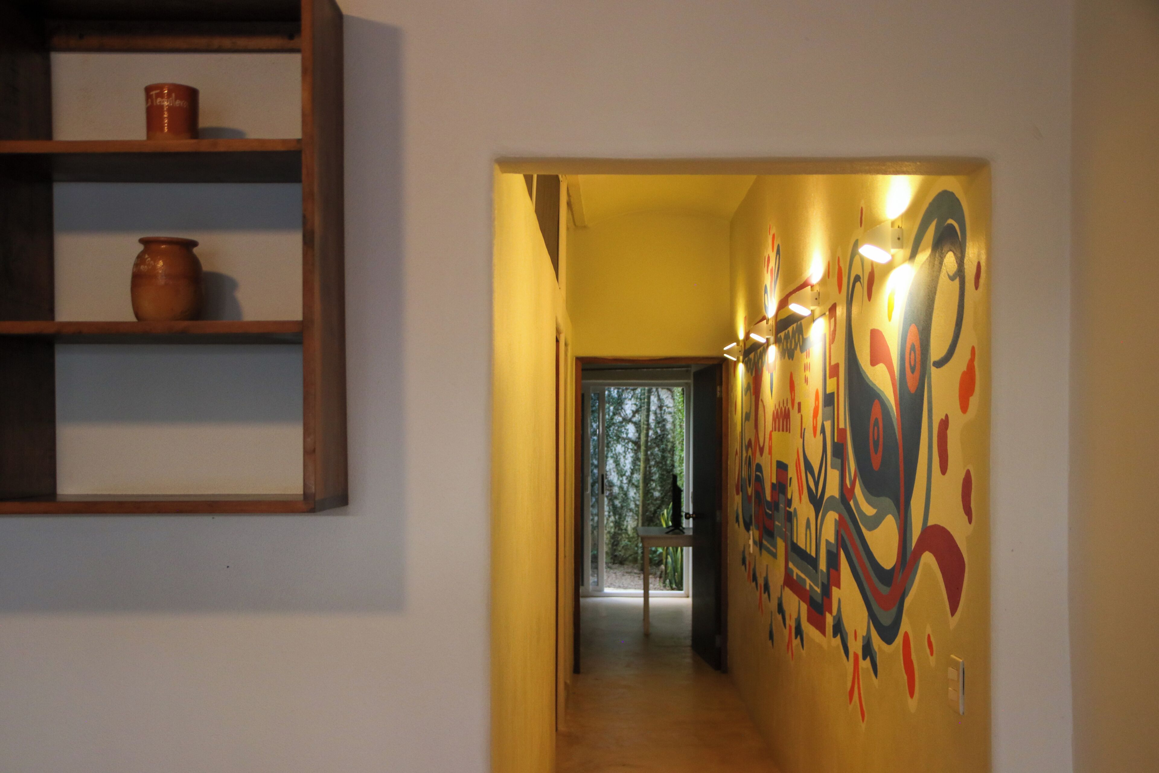 Ein Korridor mit einer Holzregal, einer Wand mit Wandgemälde und einer Tür, die auf einen Balkon führt.