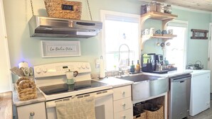 A kitchen with a stove, oven, sink, and dishwasher. There are baskets on the counter, a hanging basket above the stove, and a sign on the wall.