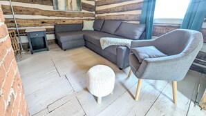A cozy room with a wooden log wall, a grey sofa, a round ottoman, and a small table.