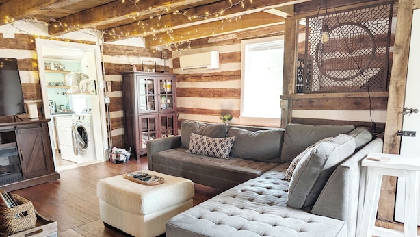 A cozy log cabin interior with a sofa, ottoman, and a kitchen area visible.