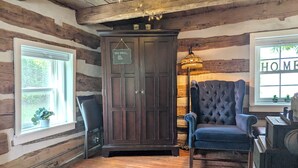 A log cabin interior with a wooden floor, a dark wooden cabinet, a blue upholstered armchair, and a chandelier.