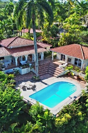 Eine Villa mit Swimmingpool, umgeben von üppiger Vegetation und Palmen.
